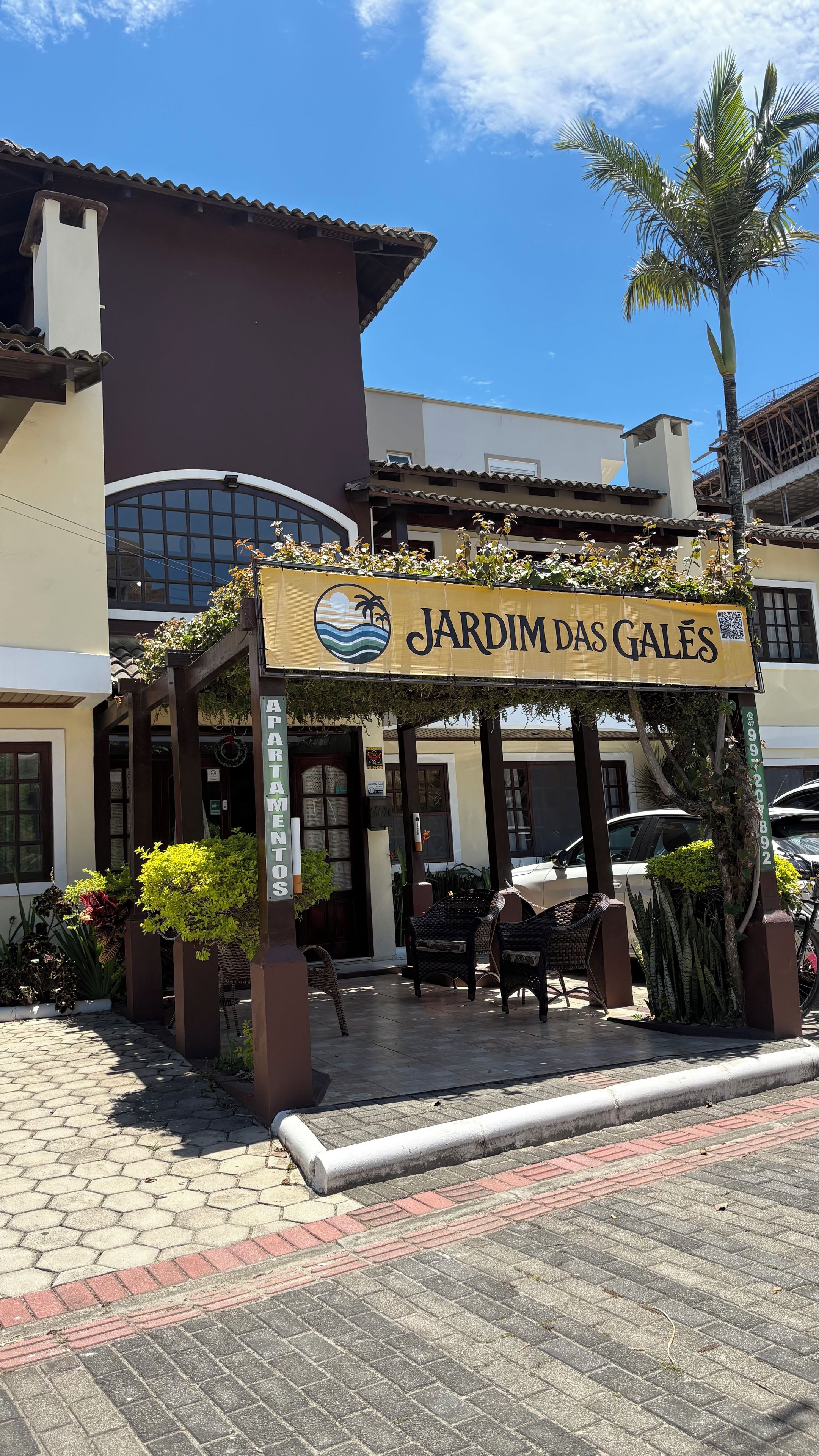 Um edifício com placa indicando 'JARDIM DAS GALÊS' e área externa coberta com cadeiras.