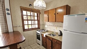 Een compacte keuken met een gasfornuis, oven, spoelbak en een witte koelkast.