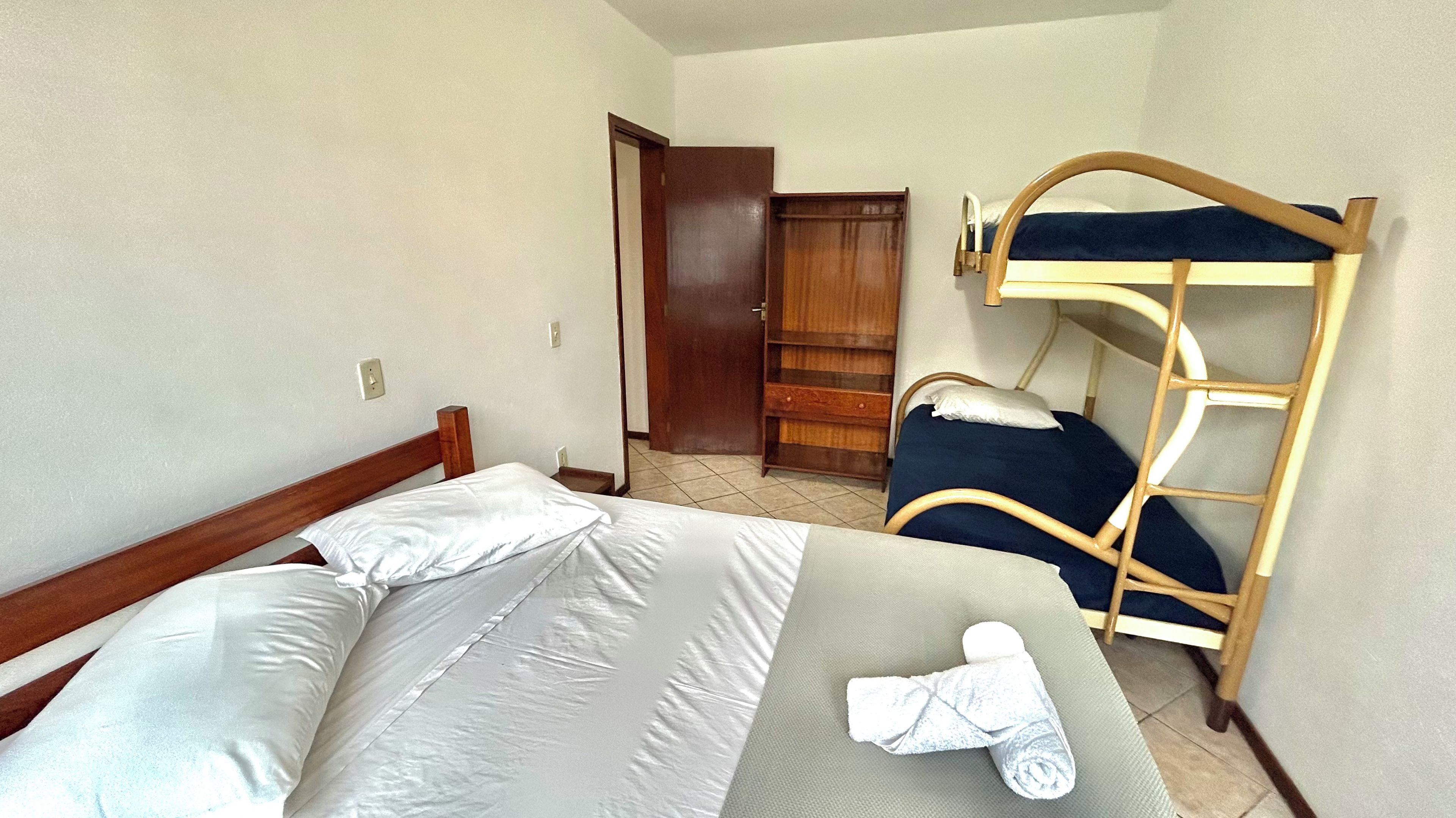 Une chambre avec un lit simple, un lit superposé, une armoire en bois et une porte donnant sur une autre pièce.