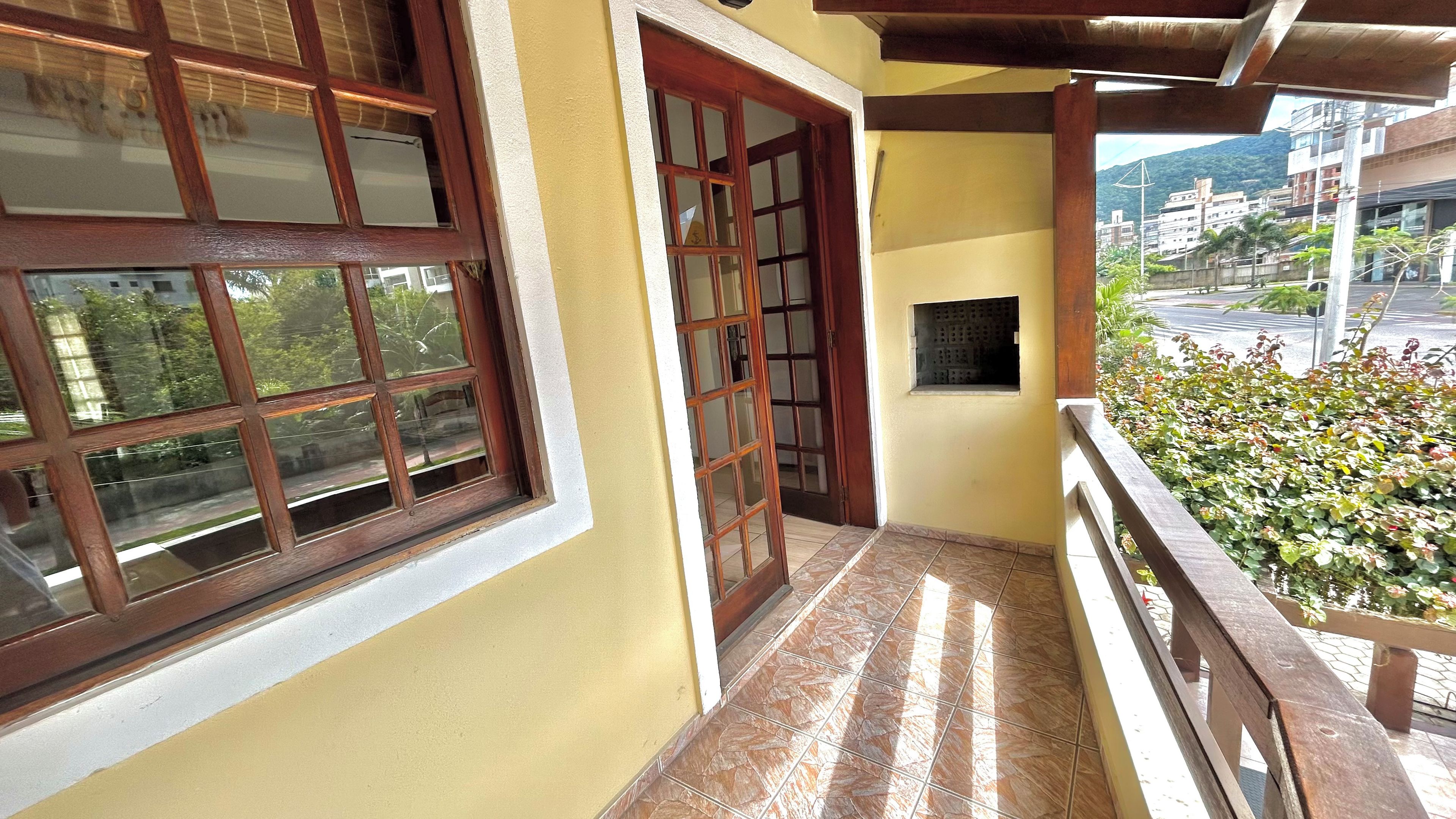 Un balcón con vistas a una calle y edificios, una puerta de madera y un ventanal con una placa.