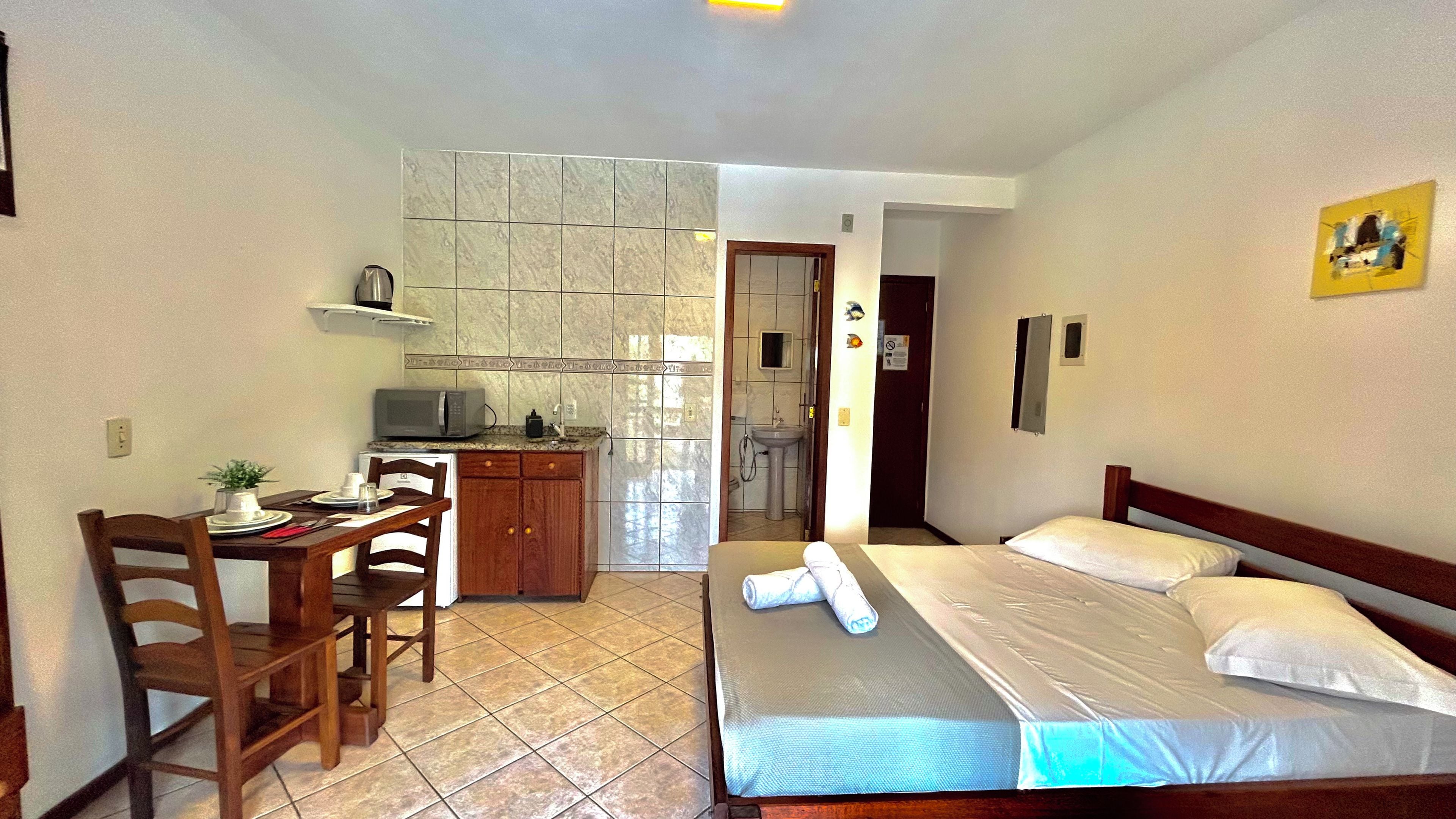 Habitación de hotel compacta con cama, kitchenette pequeña, zona de comedor y baño.
