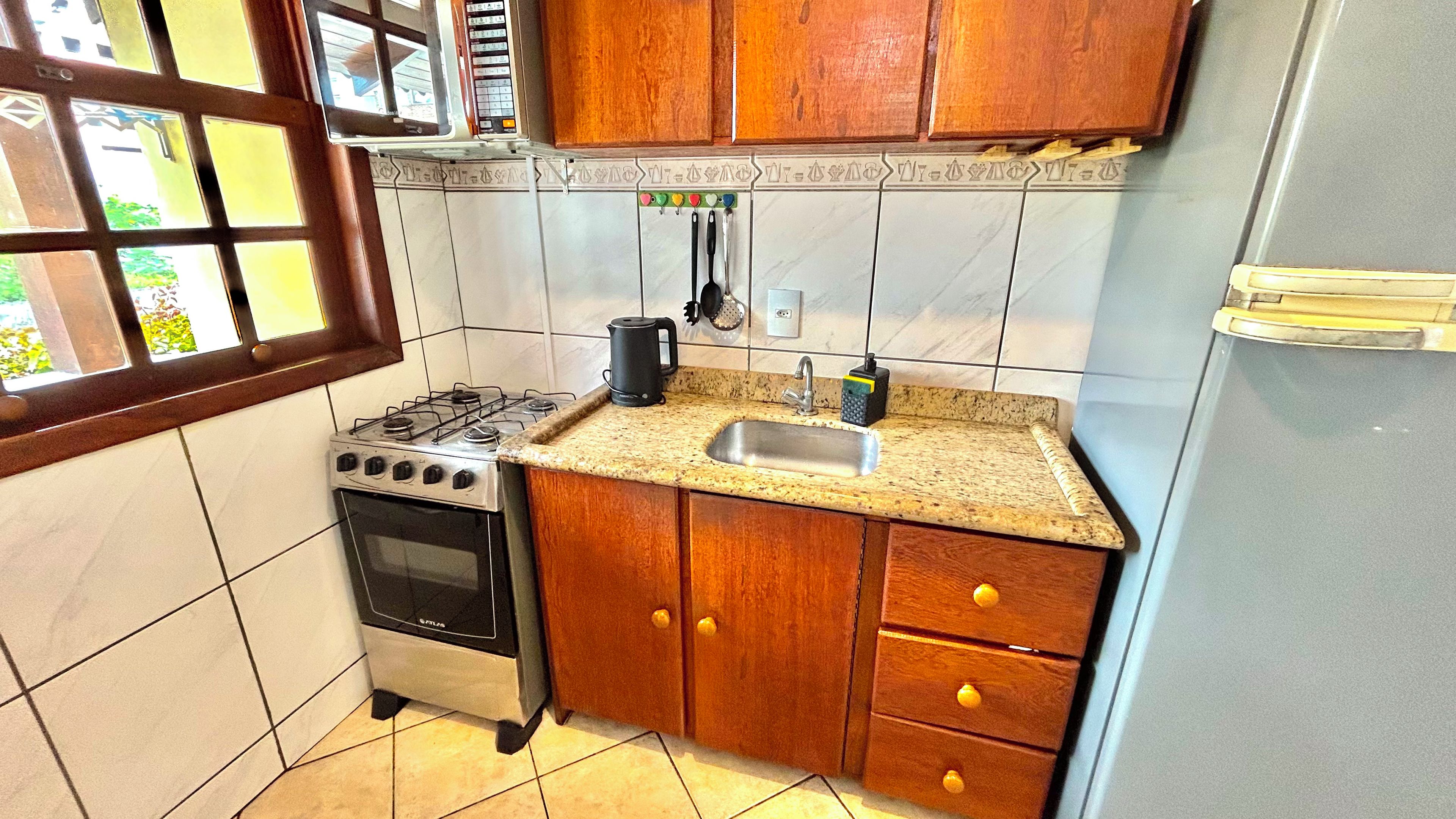 A kitchen with a gas stove, sink, wooden cabinets, and a window with a view.