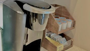 Una máquina de café con bandeja de goteo, un depósito para cápsulas de café y un recipiente para azúcar sobre una encimera.