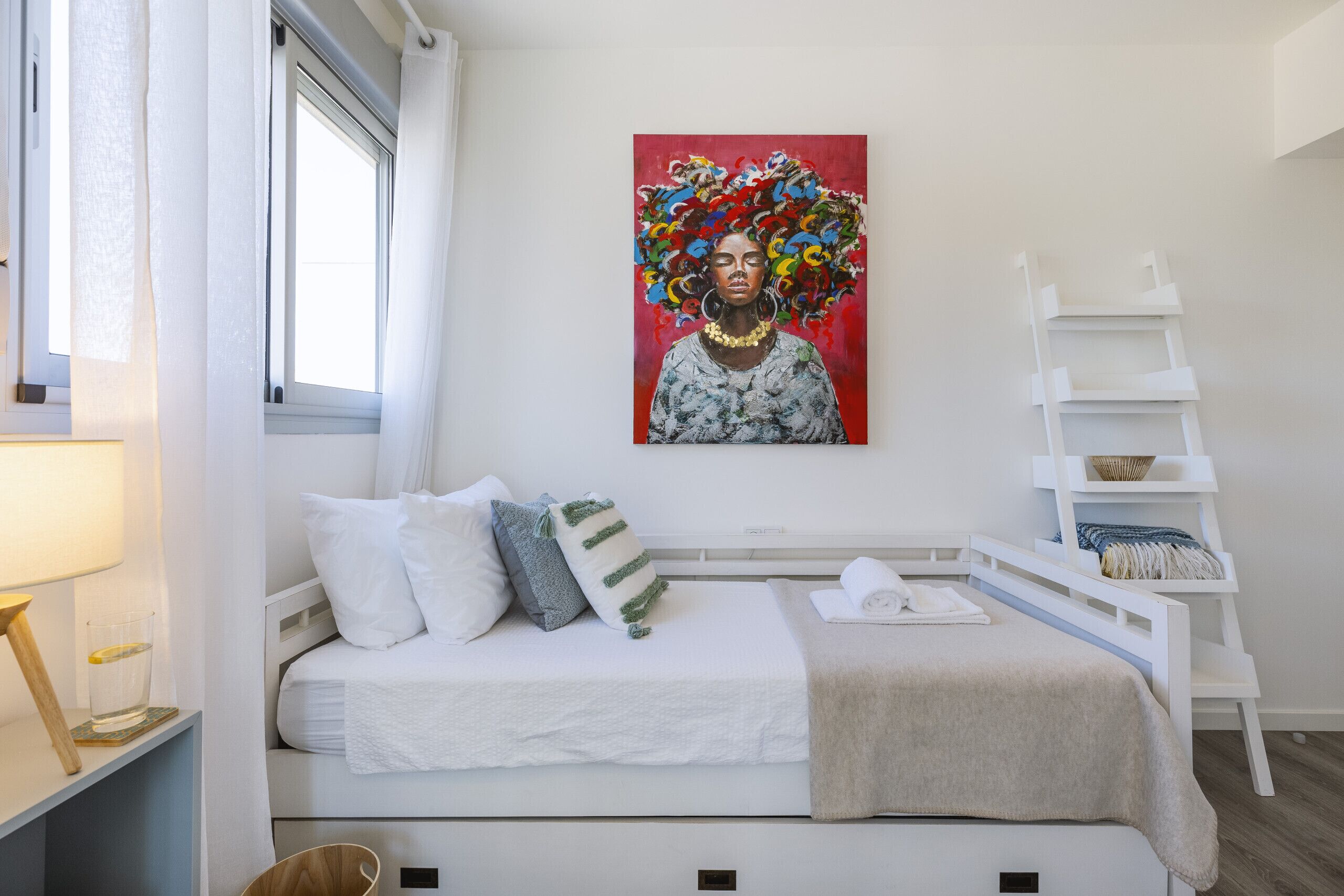Een moderne slaapkamer met een wit bed, een ladder en een schilderij aan de muur.