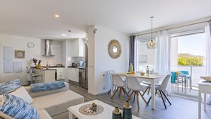 A modern apartment with a living area, dining space, and kitchen. It features a balcony with a view of the landscape.