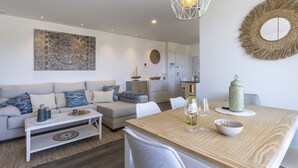 A modern living room with a sofa, coffee table, and dining table. There is a decorative wall piece and a hanging light fixture.
