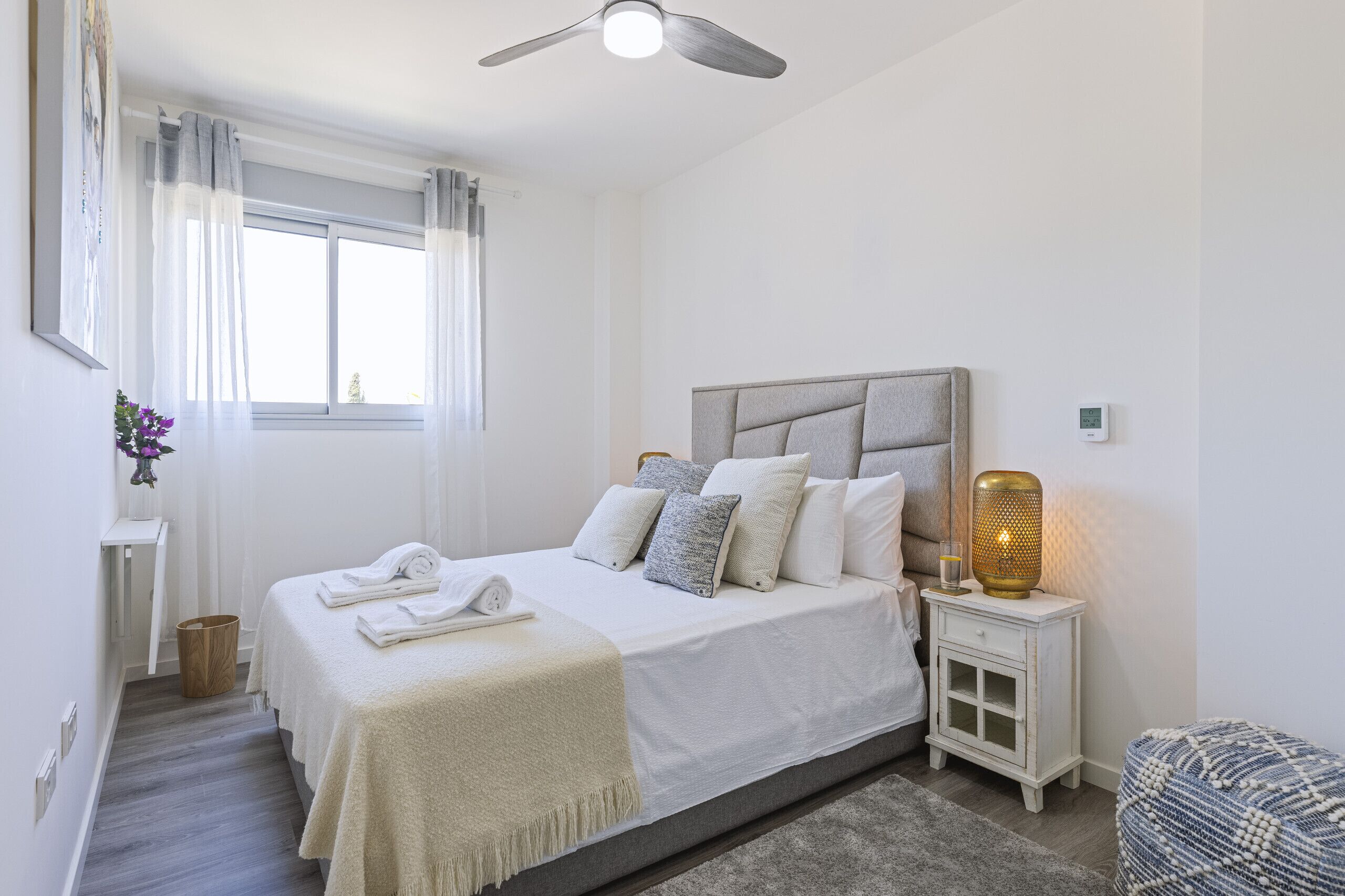 A bedroom with a bed, bedside table, nightstand, and a window with curtains.