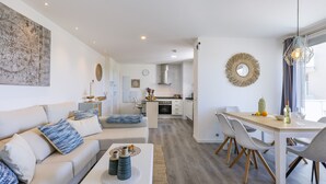 A modern living room with a sofa, dining table, and kitchen in the background.