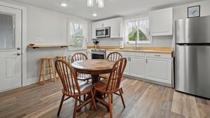 A modern kitchen with white cabinets, a stainless steel refrigerator, wooden chairs, and a round dining table.