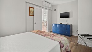 A bedroom with a bed, a blue dresser, a television, and an air conditioning unit.