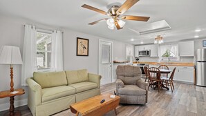 A living room with a sofa, armchair, coffee table, and a ceiling fan.