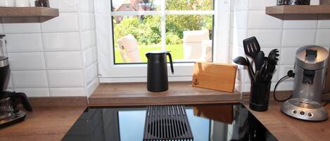 A kitchen with a black countertop, a window with a view of greenery, a coffee maker, and a kettle.