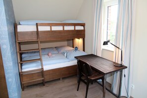 Una cama litera con escritorio y silla, una lámpara y una ventana con cortinas.