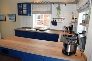 A kitchen with blue cabinets, a wooden countertop, a sink, a coffee maker, and hanging plants. - Framheim - 100qm Luxus-ferienhaus für 7 Personen Direkt am Wasser bei Greetsiel! (Krummhörn)