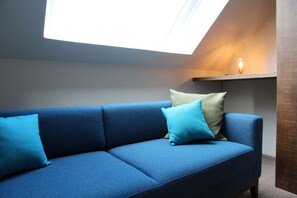 A blue sofa with cushions, a skylight, and a wall-mounted light fixture. - Framheim - 100qm Luxus-ferienhaus für 7 Personen Direkt am Wasser bei Greetsiel! (Krummhörn)