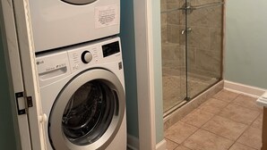 A laundry area with stacked washers and dryers, a glass shower enclosure, and a tiled floor. - Charming 2-bedroom 1 bath, Livingroom, full kitchen, WiFi & AC in Alpharetta.  (Alpharetta)