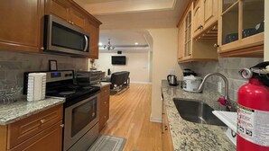A kitchen with wooden cabinets, a microwave, a stove, a sink, and a fire extinguisher. - Charming 2-bedroom 1 bath, Livingroom, full kitchen, WiFi & AC in Alpharetta.  (Alpharetta)