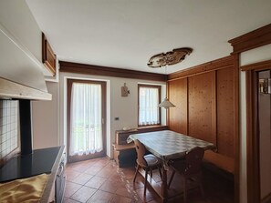 Une cuisine équipée d’une cuisinière, d’une table avec des chaises, d’une fenêtre avec des rideaux et d’une horloge au mur.