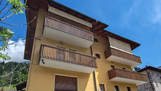 A multi-story building with balconies, a garage, and a small outdoor seating area. - Apartment 'Appartamento Nide A Vodo' with Mountain View, Private Terrace and Balcony (Vodo di Cadore)