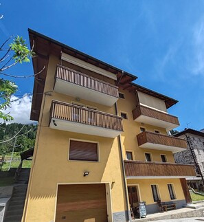 Un immeuble à plusieurs étages doté de balcons, d’un garage et d’un petit espace extérieur aménagé pour s’asseoir.