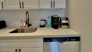 A compact kitchen with white cabinets, a stainless steel sink, a coffee maker, and a dishwasher. - Unit 7 -1 BDRM/Pool/Near Beach/Airport/Supermarket (Nassau)