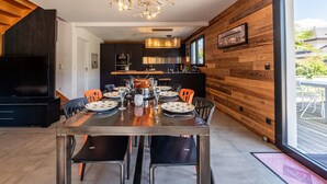A modern dining area with a wooden wall, a large window, and a chandelier.