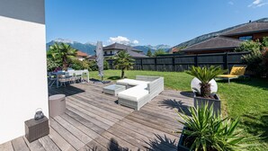 A wooden deck with outdoor furniture, a grassy yard, and a mountain backdrop.