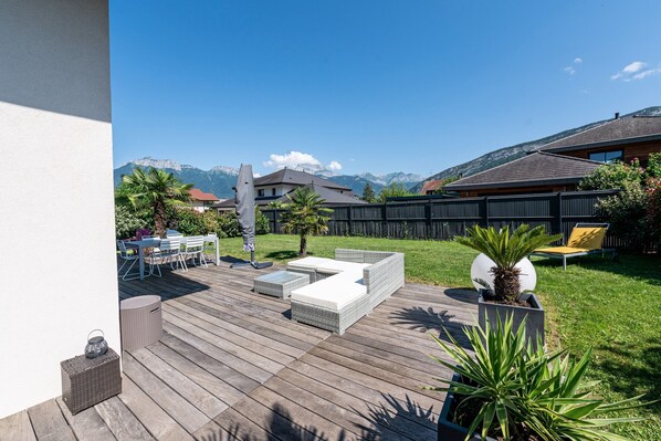 Une terrasse en bois avec des meubles d’extérieur, une pelouse et une vue sur les montagnes en toile de fond.