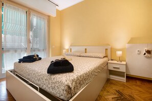Ett hotellrum med en säng, ett nattduksbord, en lampa, en väggmonterad värmare och ett fönster med gardiner.
