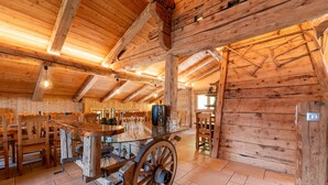 Ein rustikaler Holzinnenraum mit Holztisch und -stühlen, einem großen Holztrog und einer Holzzielendecke mit freiliegenden Balken.