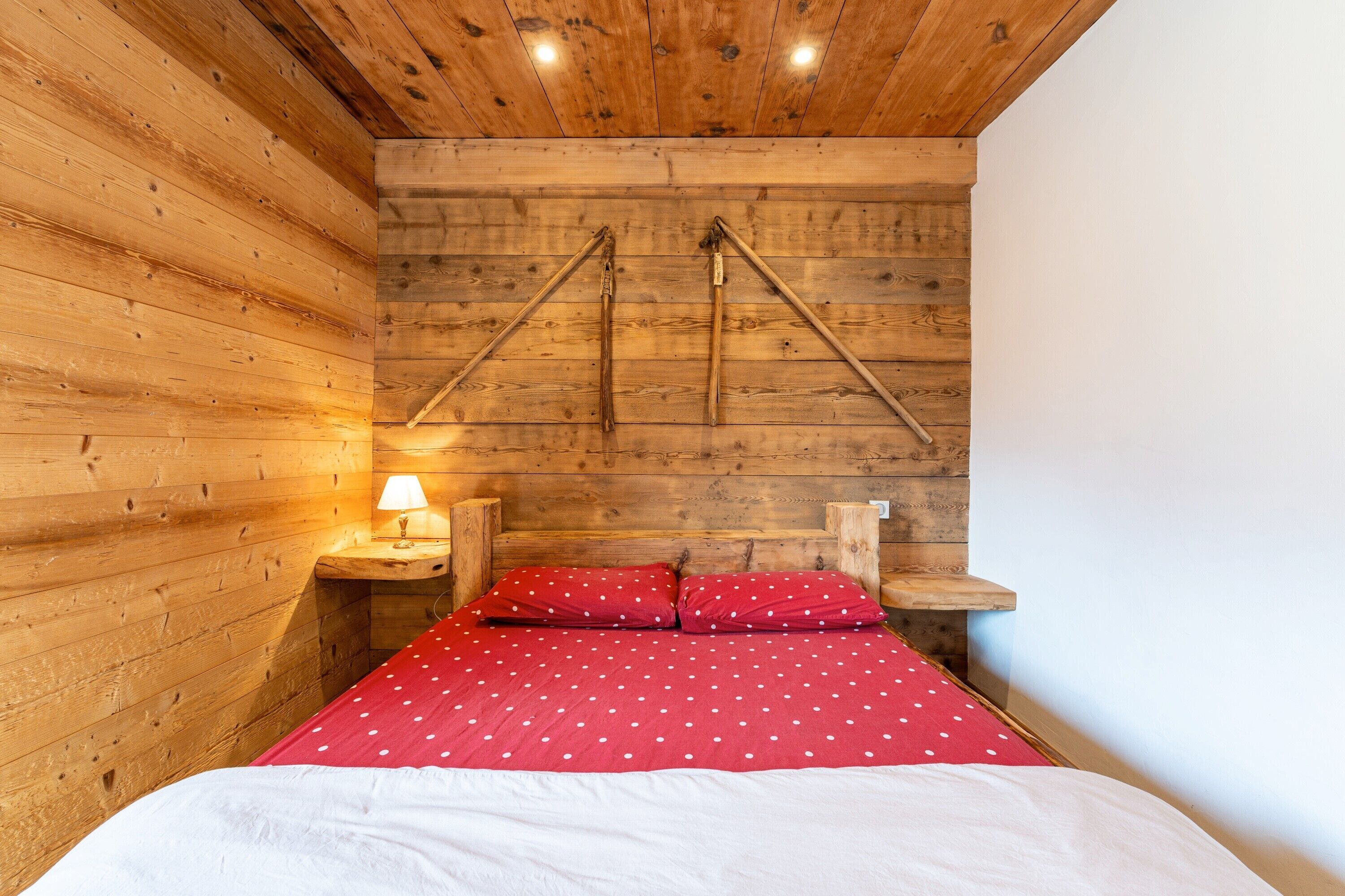 Een houten kamer met een bed, nachtkastje en een wandlamp.