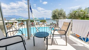 A balcony with a pool, metal chairs, and a view of the sea and mountains.