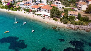 An aerial view of a coastal area with clear turquoise waters, several sailboats anchored near the shore, and a row of buildings with red-tiled roofs. - Room 'Sea View - Aeolus Building' with Shared Pool, Shared Garden and Air Conditioning (Nikiana / Lefkas)