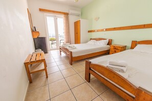Une chambre d’hôtel avec deux lits en bois, un banc en bois, une armoire et une vue sur l’extérieur, visible à travers une porte vitrée.