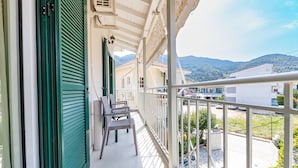 A balcony with a view of a mountainous landscape, a railing, and a door with shutters.