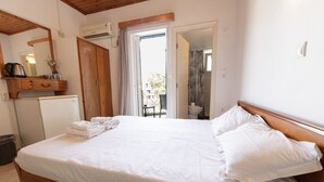 A bedroom with a bed, a wooden wardrobe, a small kitchenette, and a bathroom visible through an open door.