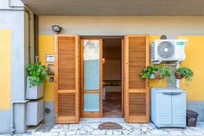 L’entrée d’un hôtel, avec des volets en bois, un appareil de climatisation et des plantes en pot.