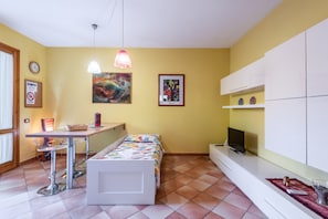 A compact room with a bed, a desk, a chair, a TV, and artwork on the walls.