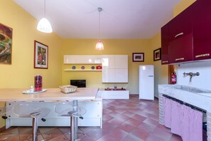 A kitchen with a dining table, chairs, a refrigerator, cabinets, and a hanging light fixture.