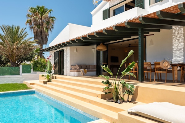 A modern house with a swimming pool, outdoor seating, and a pergola.