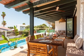 An outdoor dining area with a pool, wooden furniture, and a covered patio.