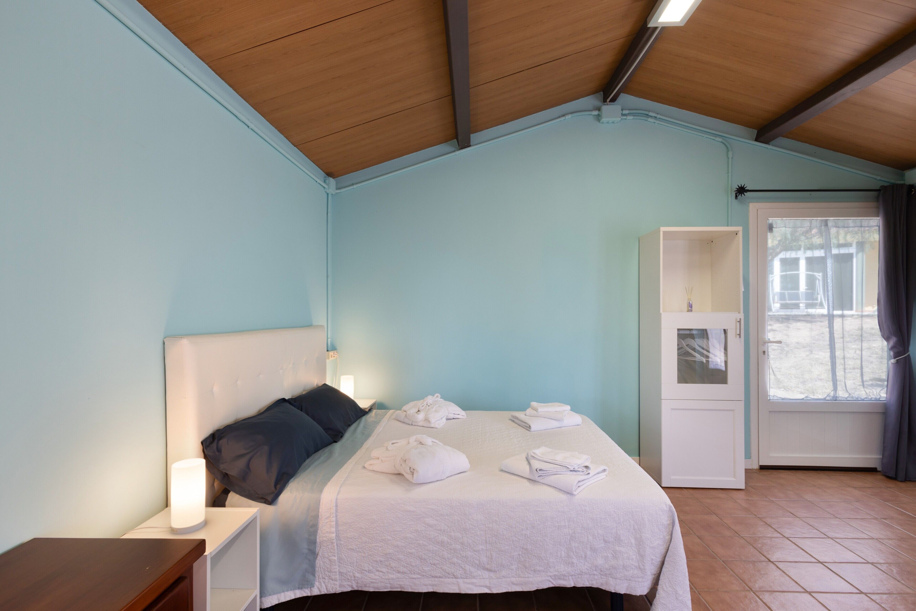 Quarto com cama, mesa de cabeceira, guarda-roupa e janela com cortinas.