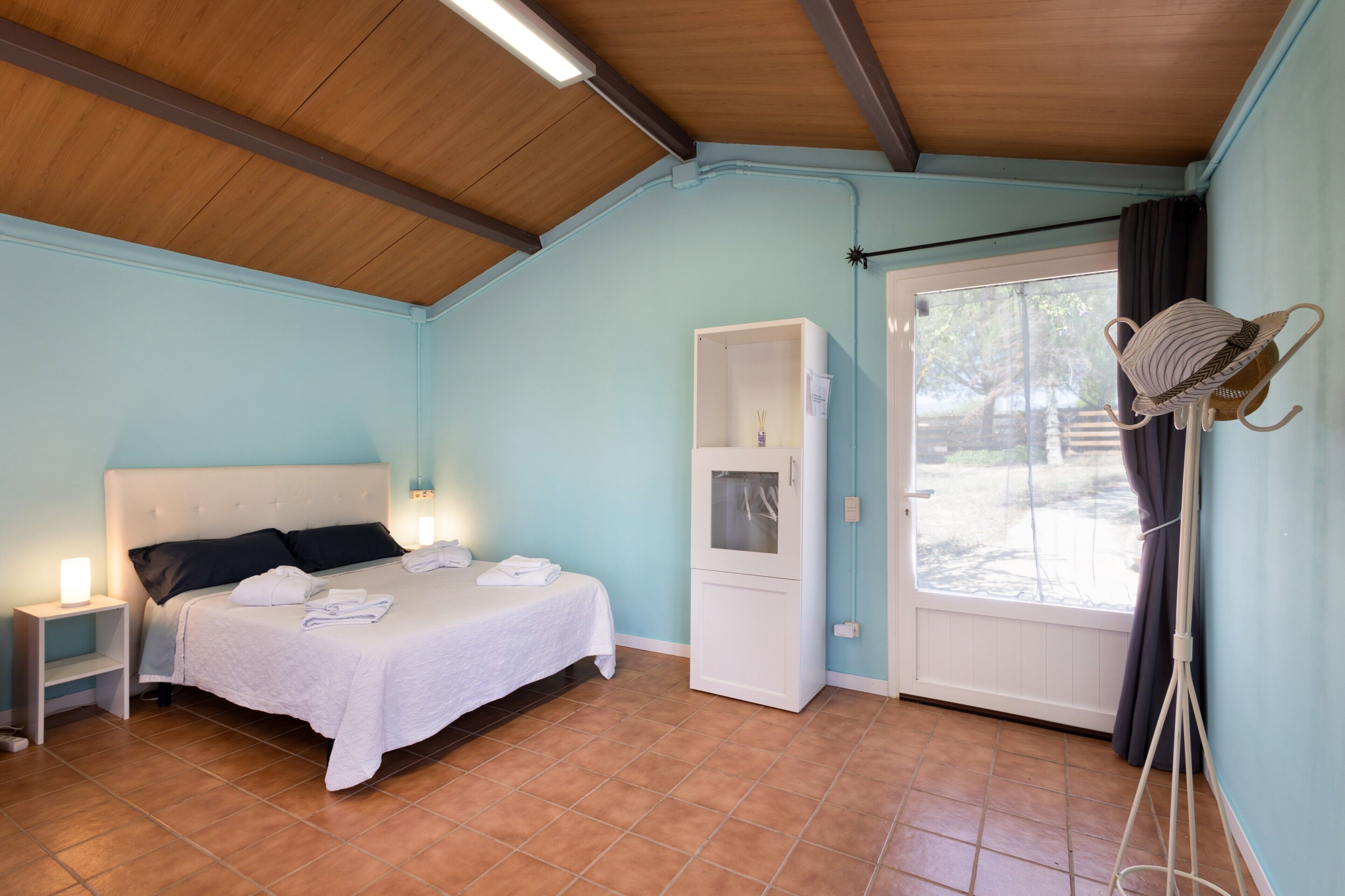 A bedroom with a bed, bedside table, wardrobe, and a window with curtains.