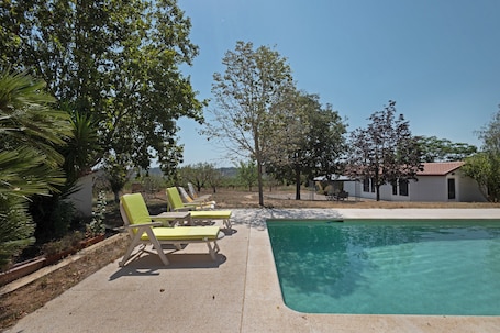 A swimming pool with lounge chairs, surrounded by trees and a building in the background.