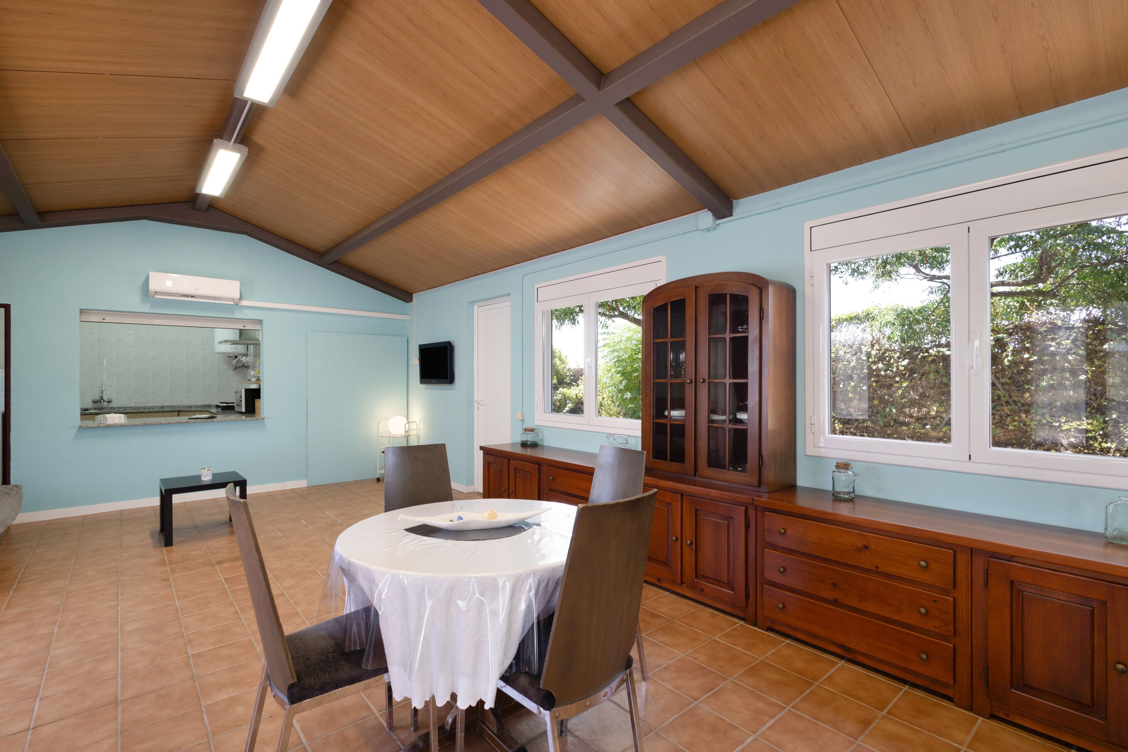 Un comedor con una mesa redonda, sillas, un mueble y una ventana con vista a árboles.