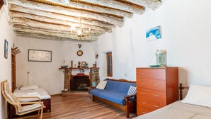 Ein Zimmer mit Holzboden, einem Bett, einem Sofa, einer Holzkommode, einem Sessel, einem Kamin und einer Wanduhr.