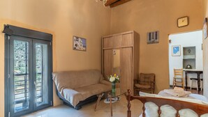 Ein Zimmer mit einer Couch, einem Holzschrank, einem Esstisch mit Stühlen und einem Bett mit Holz Kopfteil.