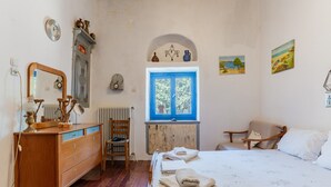 Ein Schlafzimmer mit einem hölzernen Schminktisch, einem Bett mit blauem Fenster, einem Stuhl und einer Heizung.