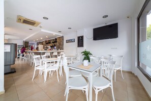 Un intérieur de restaurant moderne avec des chaises et des tables blanches, un bar et un téléviseur fixé au mur.