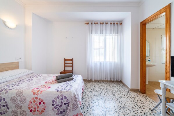 Une chambre à coucher avec un lit, une chaise, une fenêtre avec des rideaux, un lavabo et un miroir dans la salle de bain.
